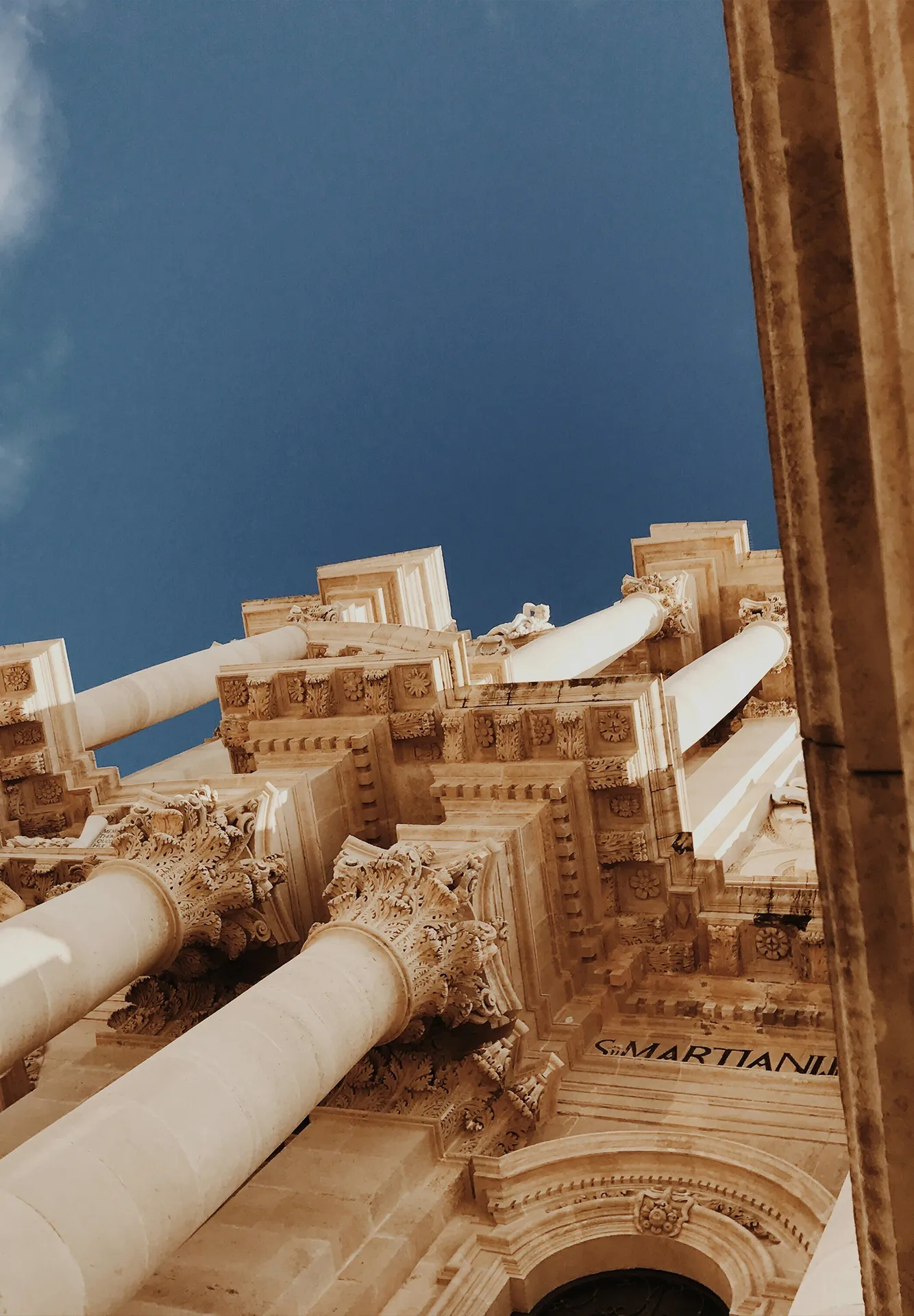 Vista dal basso della facciata barocca del Duomo di Siracusa, con le sue elaborate colonne corinzie e capitelli scolpiti.