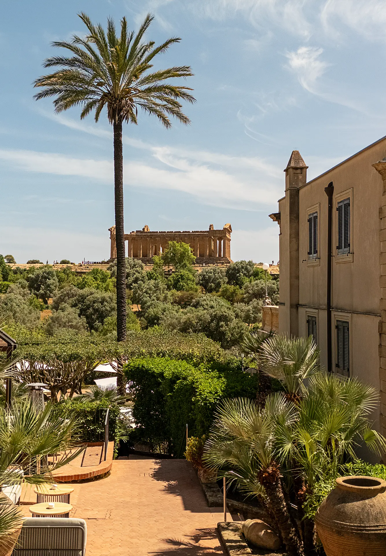 Facciata storica di Villa Athena, albergo 5 stelle, con palma alta e giardino lussureggiante, sullo sfondo il Tempio della Concordia nella Valle dei Templi.