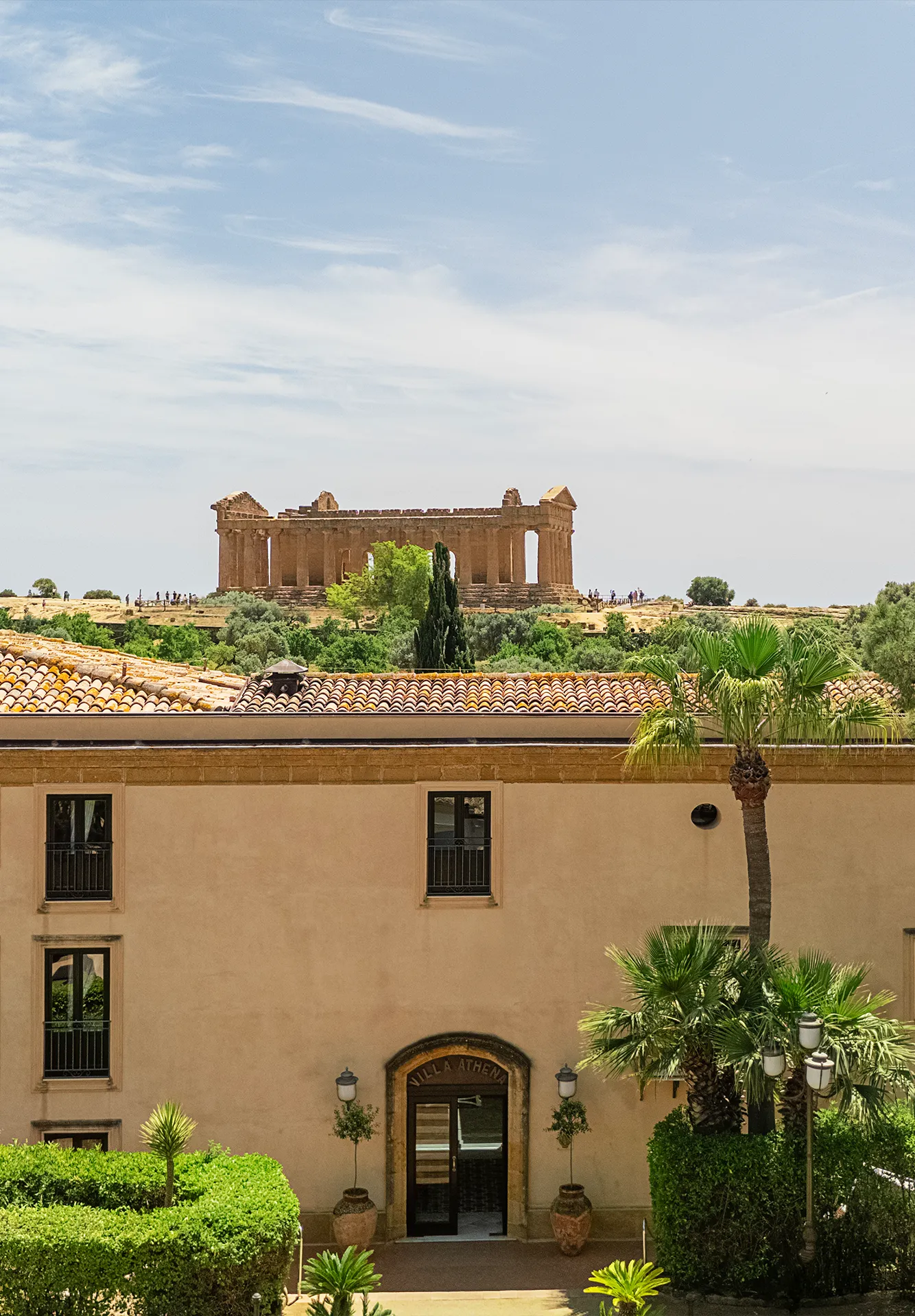 Facciata esterna della struttura con alberi, palme e vista panoramica sullo sfondo del Tempio della Concordia nella Valle dei Templi.