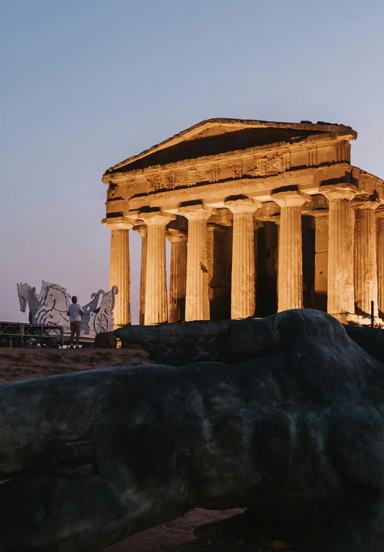 Vista del Tempio della Concordia illuminato al tramonto con la celebre statua in bronzo dell'Icaro caduto in primo piano.